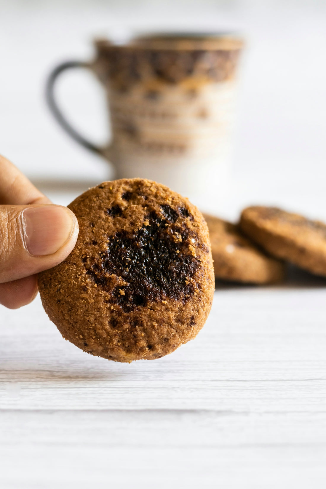 a hand holding a cookie in front of a stack of cookies