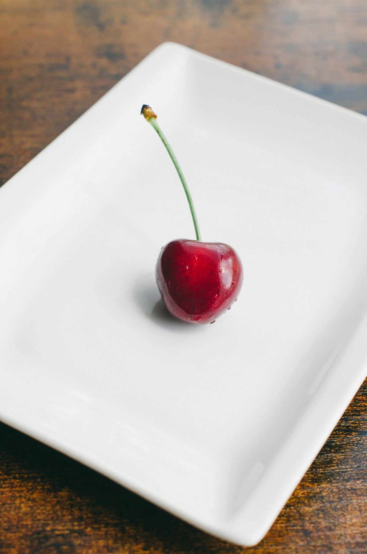 a single cherry sitting on top of a white plate